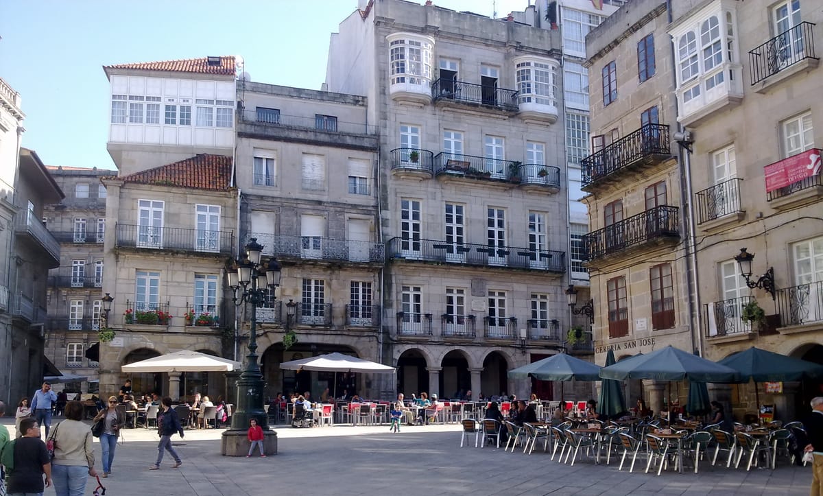 Praça do centro histórico de Vigo, com casas de pedra de varandas envidraçadas e arcadas