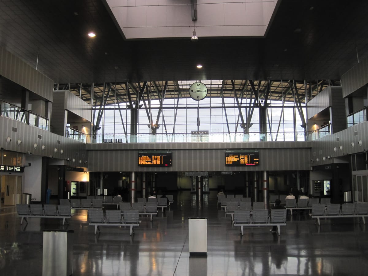 Saguão envidraçado da estação de trem de Burgos, com fileiras de cadeiras e painéis de horários