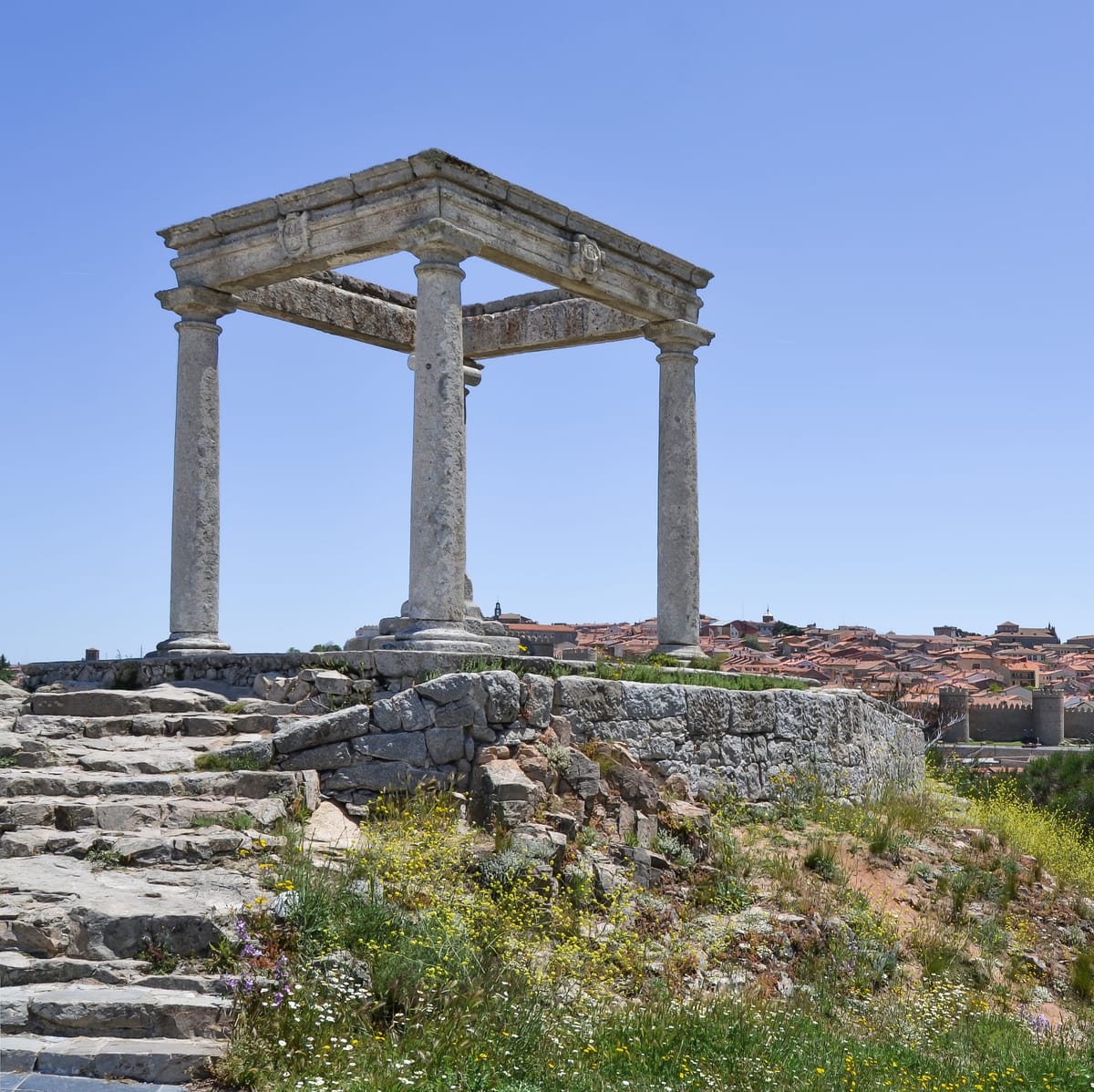 Los Cuatro Postes, quatro colunas dóricas unidas por um lintel de pedra, com a cidade murada ao fundo