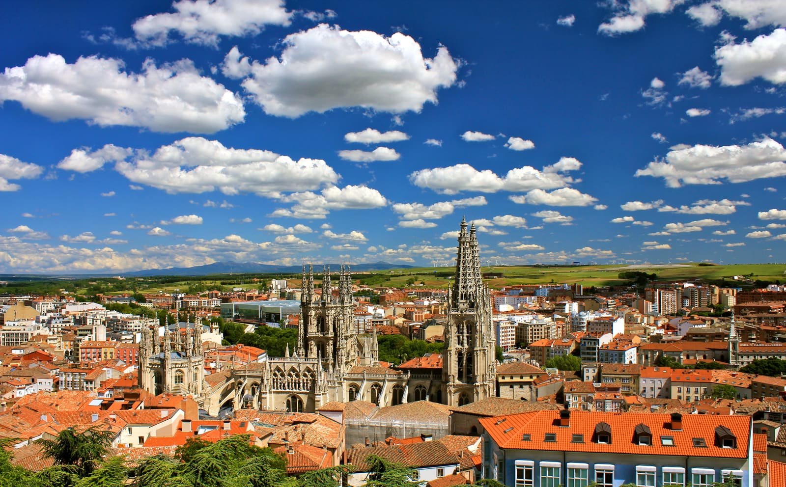 Vista de Burgos com as agulhas da catedral acima dos telhados vermelhos, sob céu azul com nuvens
