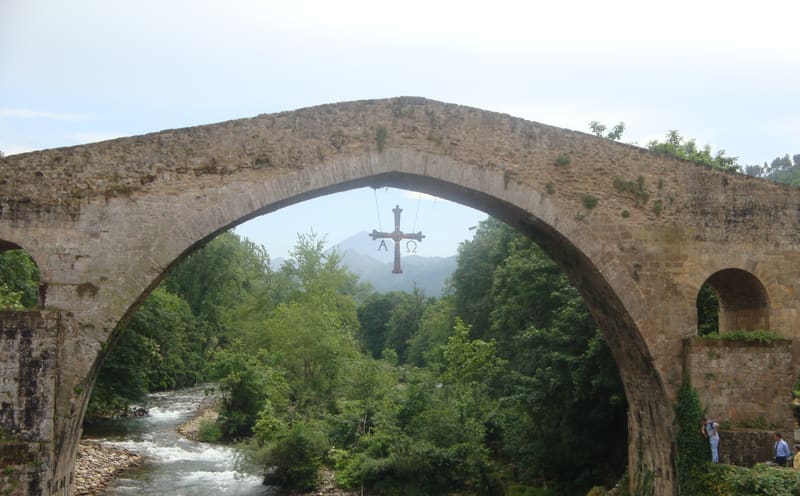 Arco central da ponte medieval de Cangas de Onís sobre o rio Sella, com a Cruz de la Victoria pendurada