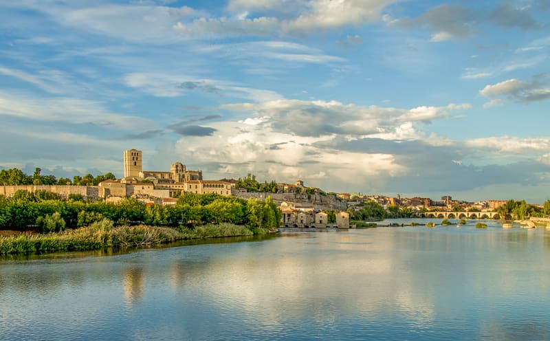 A catedral de Zamora no alto da muralha, refletida no rio Douro, com as aceñas e a ponte de pedra ao fundo